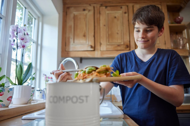 (Crédits photo : Adobe Stock - Adolescent remplissant un seau de compost avec des épluchures de légumes dans sa cuisine)