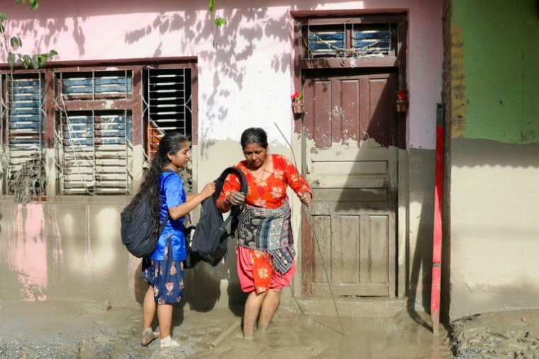 Des femmes devant une maison portant des traces de boue indiquent le niveau de l’eau après des crues dévastatrices près de Devighat, au Népal, le 27 août 2026 ( AFP / Prabin RANABHAT )