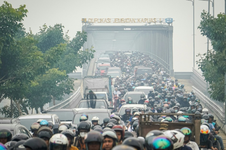 Des automobilistes et motocyclistes traversent une épaisse brume causée par des incendies de forêt et de terres sur le pont Duplikasi Jembatan Kapuas 1 à Pontianak, dans le Kalimantan occidental, le 7 octobre 2026 en Indonésie ( AFP / DITO )