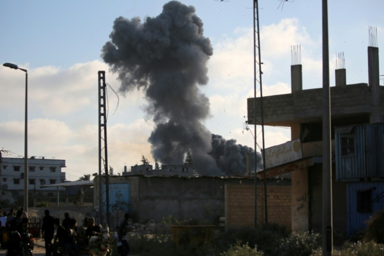 De la fumée d'une frappe israélienne alors que des Palestiniens marchent le long d'une route utilisée pour atteindre un point de distribution d'aide de la Fondation humanitaire de Gaza (GHF), près du camp de réfugiés de Nousseirat, dans le centre de la bande de Gaza, le 25 juin 2025 ( AFP / Eyad BABA )