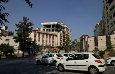 Des automobilistes passent devant un bâtiment endommagé après qu’il a été visé par une frappe israélienne dans la capitale iranienne, Téhéran, le 13 juin 2025 ( AFP / ATTA KENARE )