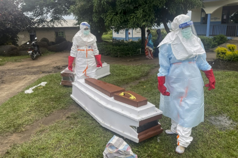 Des membres du personnel médical, en combinaisons de protection, près du cercueil d'un patient décédé du virus Ebola dans un hôpital à Rwampara, le 21 mai 2026 en RDC ( AFP / Seros MUYISA )