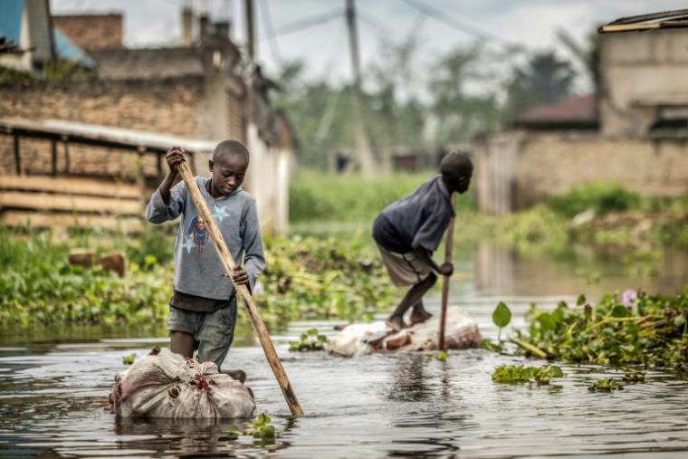Des enfants naviguent au milieu de maisons désaffectées sur des radeaux faits de bouteilles en plastique à Gatumba, au Burundi, le 9 mai 2025 ( AFP / Luis TATO )