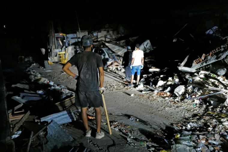 Des secouristes éclairent la zone à l'aide des phares d'un pick-up tout en recherchant d'éventuelles victimes dans un bâtiment effondré à la suite de deux séismes, à Caraballeda, dans l'Etat de La Guaira, au Venezuela, le 27 juin 2026 ( AFP / Mauricio VALENZUELA )