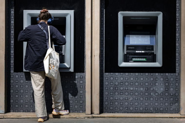 Une femme retire de l'argent à un distributeur automatique bancaire, le 3 juin 2025 à Paris ( AFP / JOEL SAGET )