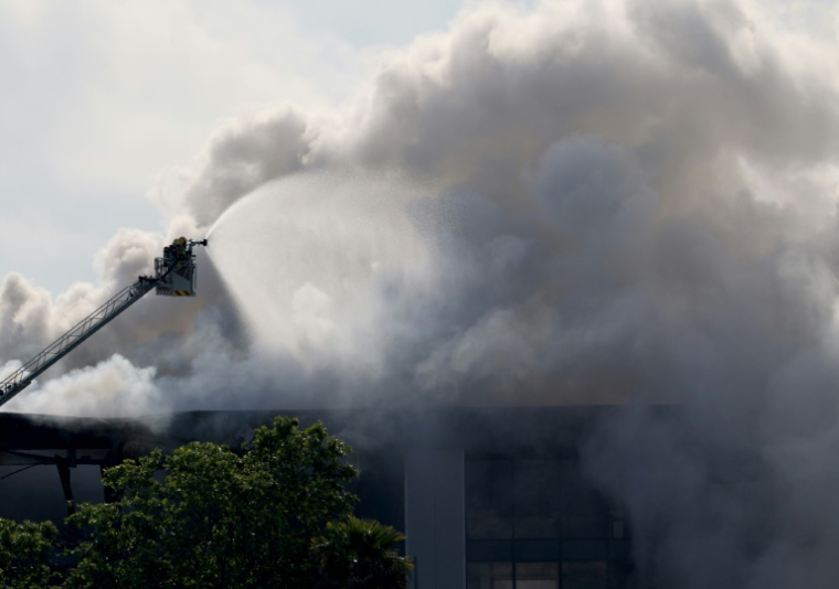 Des pompiers sur une plateforme luttent contre un incendie dans un bâtiment stockant des produits de nettoyage de piscine, dans la ville côtière de Vilanova i la Geltru, au sud de Barcelone, le 10 mai 2025 ( AFP / LLUIS GENE )