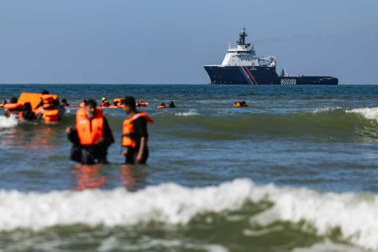 Des migrants tentent de monter à bord d'un bateau de passeurs au large de la plage d'Equihen-Plage, dans le nord de la France, tandis qu'au loin patrouille l'Abeille Normandie, remorqueur français d'urgence, le 23 septembre 2026 ( AFP / Sameer Al-DOUMY )