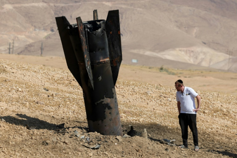 Un Israélien inspecte une roquette tombée, à moitié enfouie dans le sol, en périphérie de Jéricho en Cisjordanie, le 8 juin 2026 ( AFP / Ahmad GHARABLI )
