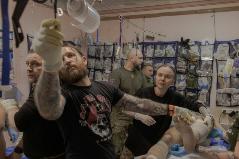 Anastassia Podobaïlo (d), son collègue et époux Mykola Iassinenko (2e g) et d'autres médecins militaires, soignent un soldat blessé dans un poste médical de la 56e brigade, dans la région de Donetsk, le 15 mars 2026 en Ukraine ( AFP / Roman PILIPEY )