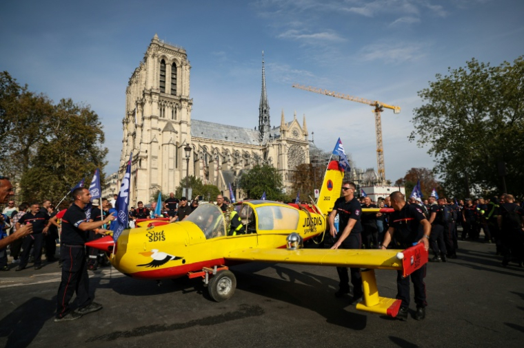 Des sapeurs-pompiers installent, devant la cathédrale Notre-Dame de Paris, un avion bombardier d'eau hors service, peint aux couleurs de la Sécurité civile et piloté par un squelette humain, lors d'une manifestation, le 28 septembre 2026 ( AFP / Xavier GALIANA )