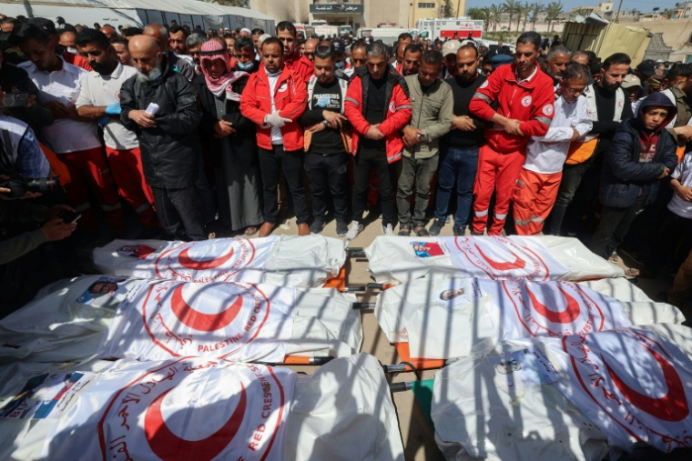 Des membres du Croissant-Rouge et d'autres secouristes se recueillent sur les dépouilles de leurs collègues tués une semaine plus tôt par des tirs israéliens, lors d'une cérémonie à Khan Younès, dans le sud de la bande de Gaza, le 31 mars 2025 ( AFP / Eyad BABA )