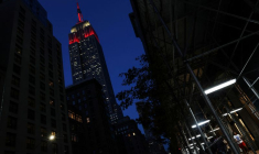 L'Empire State Building est illuminé en rouge alors que des personnes marchent dans le quartier de Midtown à New York
