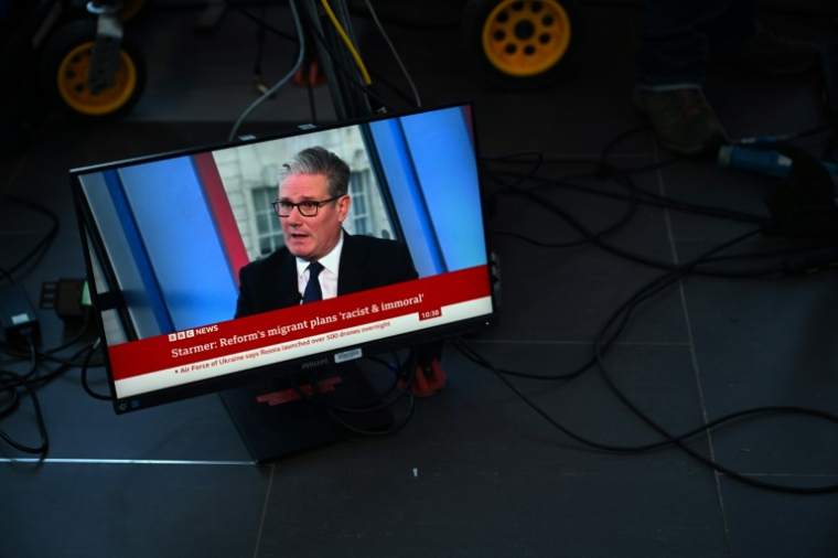 Un écran de télévision retransmet une interview de la BBC avec le Premier ministre britannique Keir Starmer et le titre "Starmer : Les plans migratoires de la réforme sont « racistes et immoraux" au premier jour de la conférence annuelle du Parti travailliste à Liverpool, dans le nord-ouest de l'Angleterre, le 28 septembre 2025 ( AFP / Paul ELLIS )