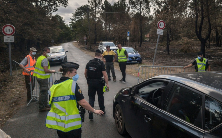 Des gendarmes filtrent des véhicules sur une route menant à la commune de Le Porge, en Gironde, ravagée par un incendie, le 31 juillet 2026  ( AFP / Ed JONES )