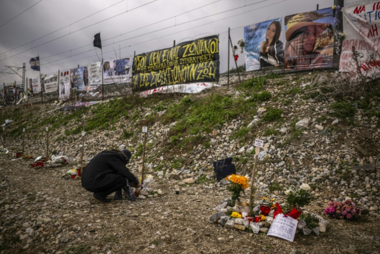 Une femme accroupie devant des hommages aux victimes de l'accident de train de Tempé, le 28 février 2024 près de Larissa, en Grèce ( AFP / Angelos TZORTZINIS )