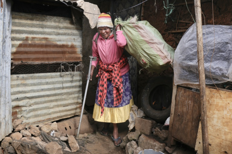 Molly Aluoch s'appuie sur une béquille pour porter un sac de déchets plastiques usagés collectés dans le bidonville de Kibera, à Nairobi, le 11 août 2025 au Kenya ( AFP / Tony KARUMBA )
