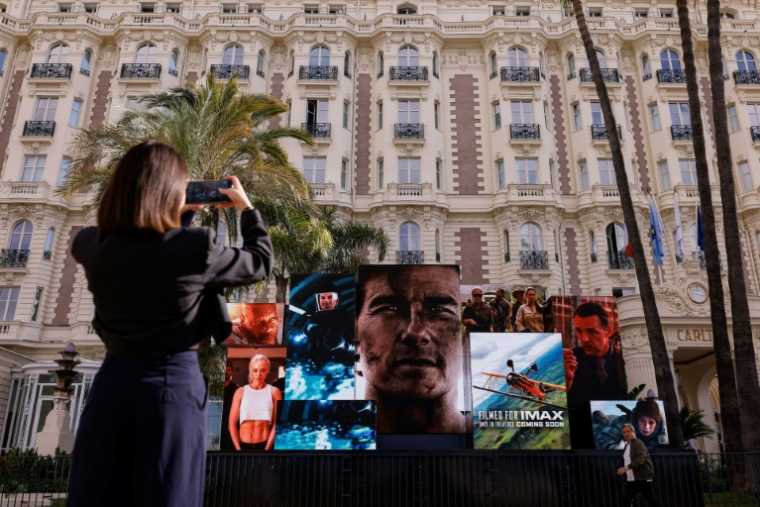 Une femme prend une photo d'un écran géant faisant la promotion du film "Mission : Impossible - The Final Reckoning" avec l'acteur américain Tom Cruise devant l'hôtel Carlton, à Cannes, dans le sud de la France, le 13 mai 2025 ( AFP / Ian LANGSDON )