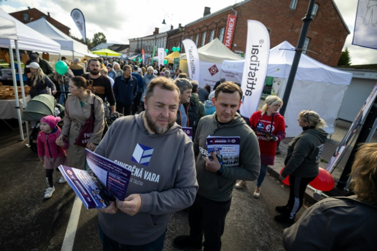 Vyacheslav Stepanenko, à gauche de l'image, candidat du parti Suverena Vara (Pouvoir souverain), distribue des tracts électoraux lors de la fête des récoltes à Rezekne, en Lettonie, le 27 septembre 2026 ( AFP / Wojtek RADWANSKI )