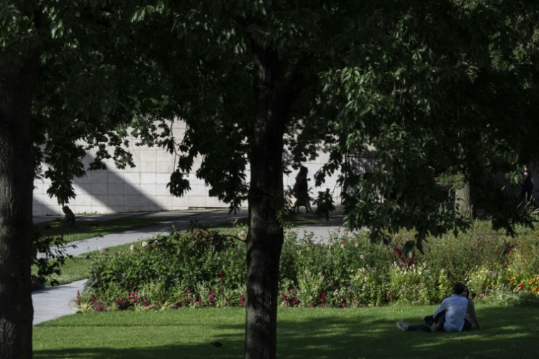 Des promeneurs sont assis à l'ombre des arbres du parc André Citroën à Paris le 12 août 2025, en pleine canicule ( AFP / Martin LELIEVRE )