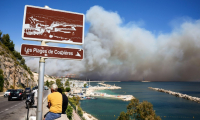 la plage des Corbières, à Marseille, dans le sud de la France, le 8 juillet 2025, des passants observent la fumée d'un incendie de forêt qui fait rage en arrière-plan ( AFP / Clement MAHOUDEAU )