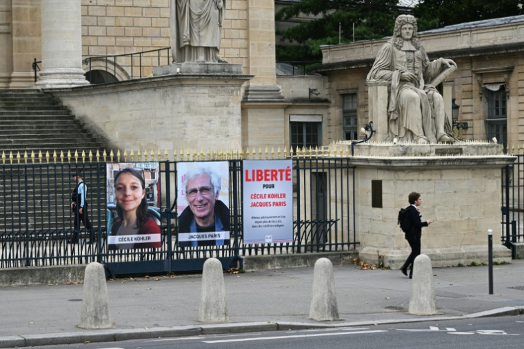 Des portraits de Cécile Kohler et de Jacques Paris, détenus en Iran, installés sur une grille de l'Assemblée nationale à Paris, le 6 octobre 2025 ( AFP / Martin LELIEVRE )