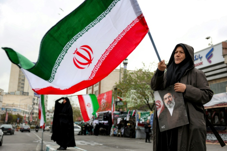 Une femme tient une photo du nouveau guide suprême iranien, Mojtaba Khamenei, et un drapeau national sur la place Enghelab à Téhéran, le 25 mars 2026 ( AFP / - )