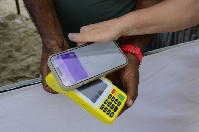 Une femme règle un achat sur la plage de Copacabana à l'aide du système de paiement instantané brésilien PIX, à Rio de Janeiro, le 9 juillet 2026 au Brésil ( AFP / Pablo PORCIUNCULA )