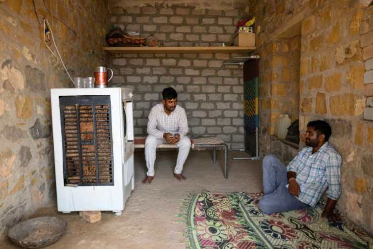 Deux hommes devant un climatiseur, par 42°C, le 29 mai 2026 à Sanwata, au Rajasthan, en Inde ( AFP / Manan VATSYAYANA )