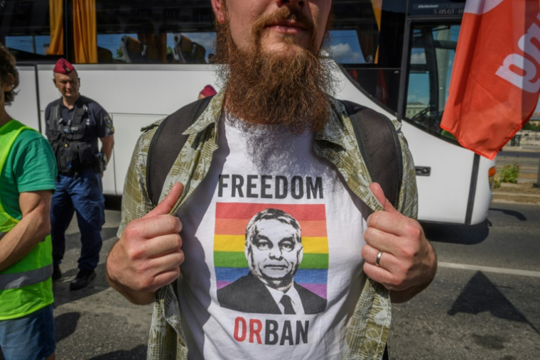 Un manifestant montre un portrait du Premier ministre hongrois Viktor Orban sur fond de drapeau LGBT+, imprimé sur son t-shirt, lors d'un rassemblement contre un projet de loi ciblant les médias et les ONG, le 1er juin 2025 à Budapest ( AFP / Ferenc ISZA )