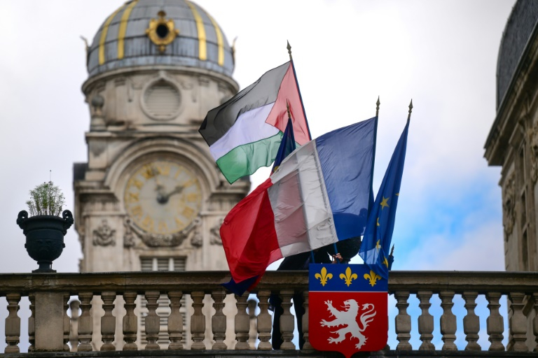 Un employé de la mairie place le drapeau palestinien à côté du drapeau français, du drapeau de Lyon et du drapeau de l'Union européenne, sur l'entrée de l'hôtel de ville de Lyon, le 22 septembre 2025 ( AFP / OLIVIER CHASSIGNOLE )