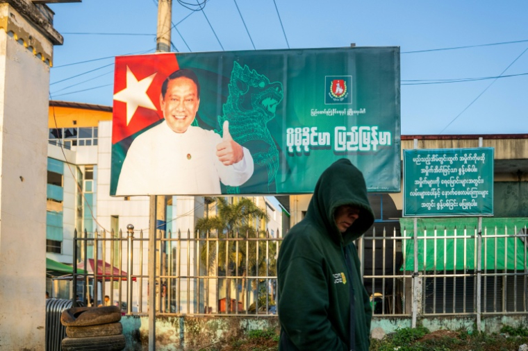 Cette photo prise le 20 décembre 2025 montre un homme passer devant un panneau de campagne de Khin Yi, de l'Union pour la solidarité et le développement, dans la région de Shan en Birmanie ( AFP / STR )