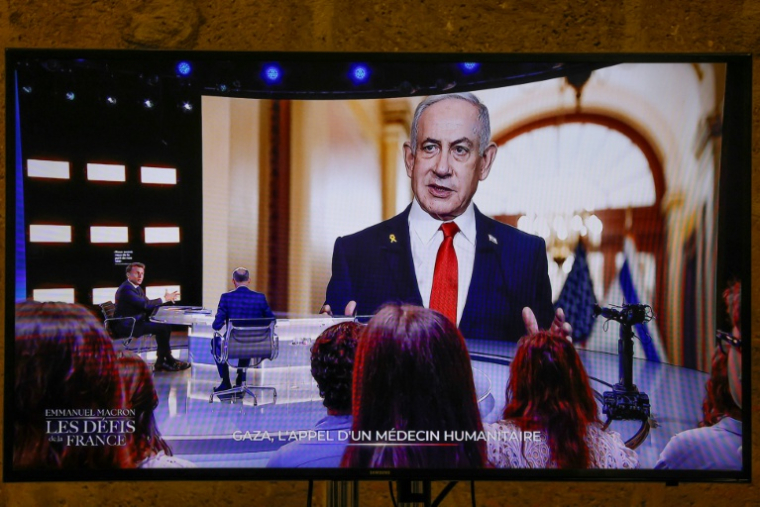 Cette photo prise sur un écran de TF1, montre le président français Emmanuel Macron, alors qu'une photo du Premier ministre israélien Benjamin Netanyahu s'affiche en arrière-plan, lors d'une émission dans les studios de télévision de Saint-Denis, le 13 mai 2025 ( AFP / Ludovic MARIN )