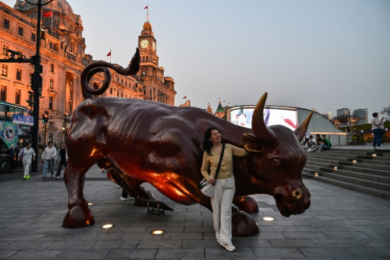 Une femme pose pour une photo à côté d'une sculpture de taureau sur le Bund à Shanghai, le 9 avril 2025 ( AFP / HECTOR RETAMAL )