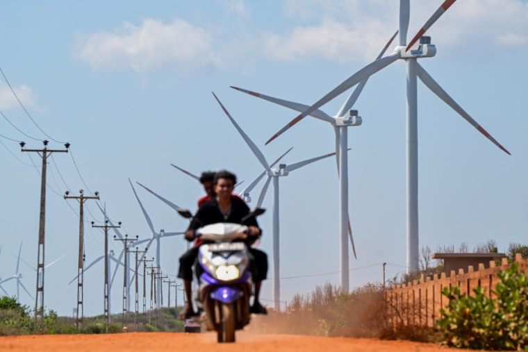 Cette photo, prise le 2 octobre 2026, montre un motard passant devant des éoliennes installées le long d'une route de la péninsule de Mannar, au Sri Lanka ( AFP / Ishara S. KODIKARA )