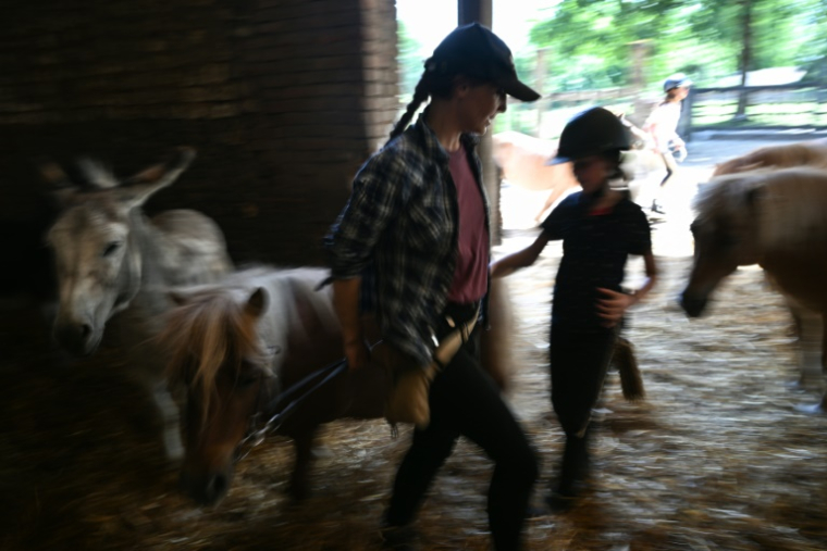 Agathe de Pas, qui a repris avec deux de ses frères la ferme équestre de Bois Guilbert, en Seine-Maritime, aide des enfants à guider leur poney, le 1er juillet 2025 ( AFP / Lou BENOIST )