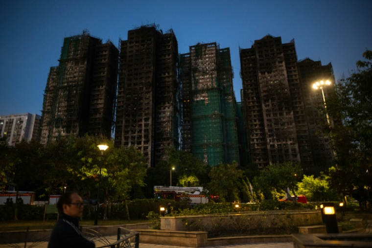 Un homme passe devant les immeubles du complexe résidentiel de Wang Fuk Court, ravagé par un incendie géant , dans le district de Tai Po à Hong Kong, le 28 novembre 2025 ( AFP / Philip FONG )