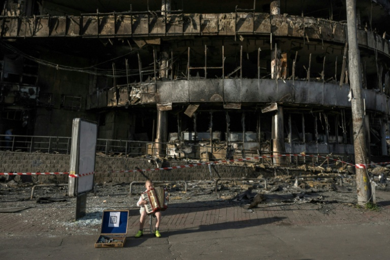 Un enfant joue de l'accordéon devant un centre commercial détruit à Kiev en Ukraine le 25 mai 2026 ( AFP / Vladyslav Musiienko )