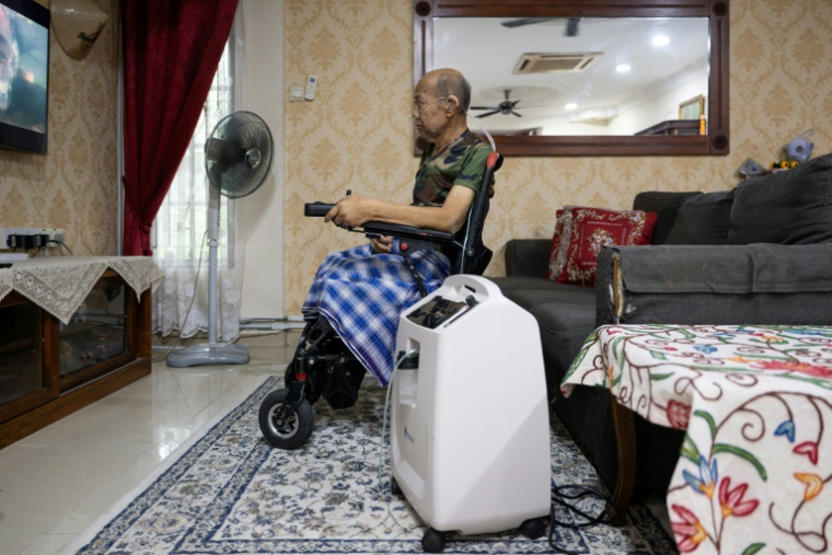 MMd Noor Bin Bujang regarde la télévision près d'un concentrateur d’oxygène à son domicile de Rawang, dans l’État de Selangor, le 16 octobre 2026 en Malaisie ( AFP / Mohd Rasfan )