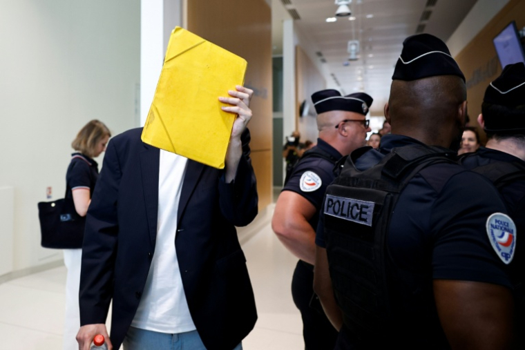 David G., animateur périscolaire, se cache le visage avec un dossier à son arrivée au tribunal où il doit être jugé pour agressions sexuelles sur neuf enfants, le 26 mai 2026 ( AFP / SIMON WOHLFAHRT )