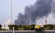 Un livreur de repas circule près d'un panache de fumée au-dessus du port Zayed après une frappe iranienne présumée à Abou Dhabi, le 1er mars 2026 aux Emirats arabes unis ( AFP / Ryan Lim )