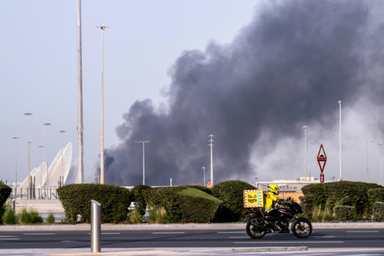 Un livreur de repas circule près d'un panache de fumée au-dessus du port Zayed après une frappe iranienne présumée à Abou Dhabi, le 1er mars 2026 aux Emirats arabes unis ( AFP / Ryan Lim )
