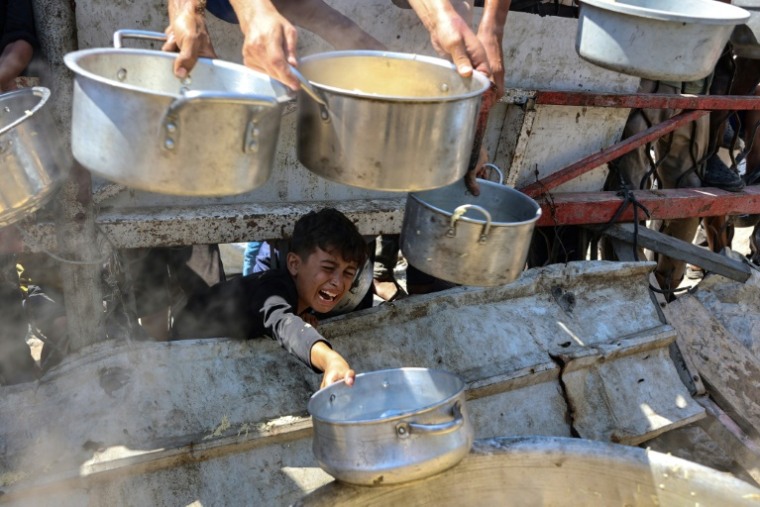 Un garçon palestinien tend une casserole vide devant une organisation de charité locale distribuant du riz cuit, dans la ville de Gaza, le 23 août 2025 ( AFP / Omar AL-QATTAA )