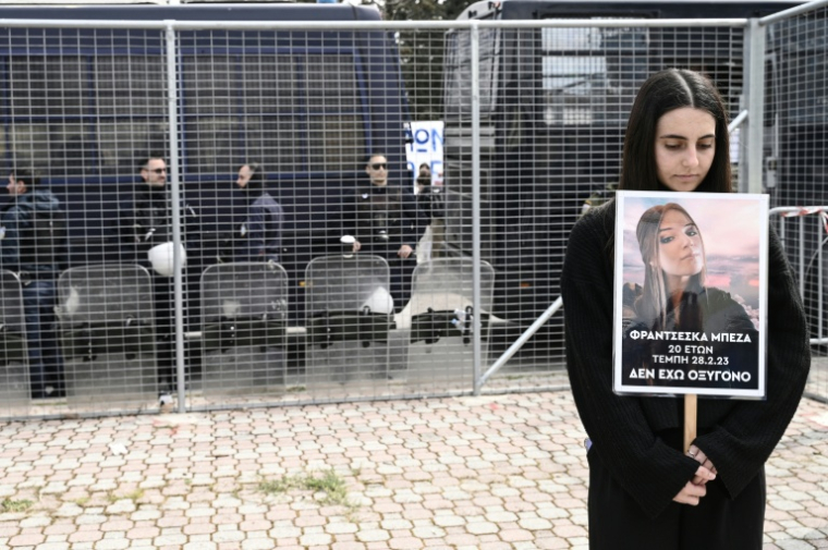 Une femme porte le portrait d'une proche décédée dans la collision ferroviaire la plus meurtrière de Grèce alors que s'ouvre le procès de 36 personnes, le 23 mars 2026 sur le campus universitaire de Larissa ( AFP / Sakis Mitrolidis )