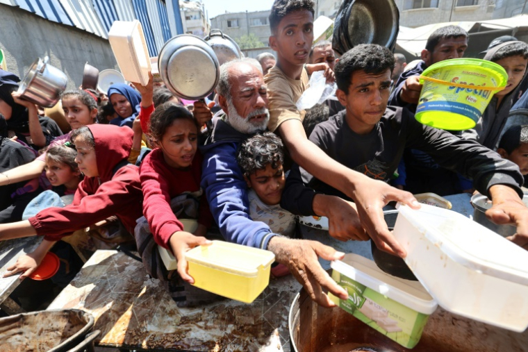 Des Palestiniens font la queue pour obtenir un repas chaud lors d'une distribution alimentaire au camp de réfugiés de Nousseirat, dans le centre de la bande de Gaza, le 4 mai 2025 ( AFP / Eyad BABA )