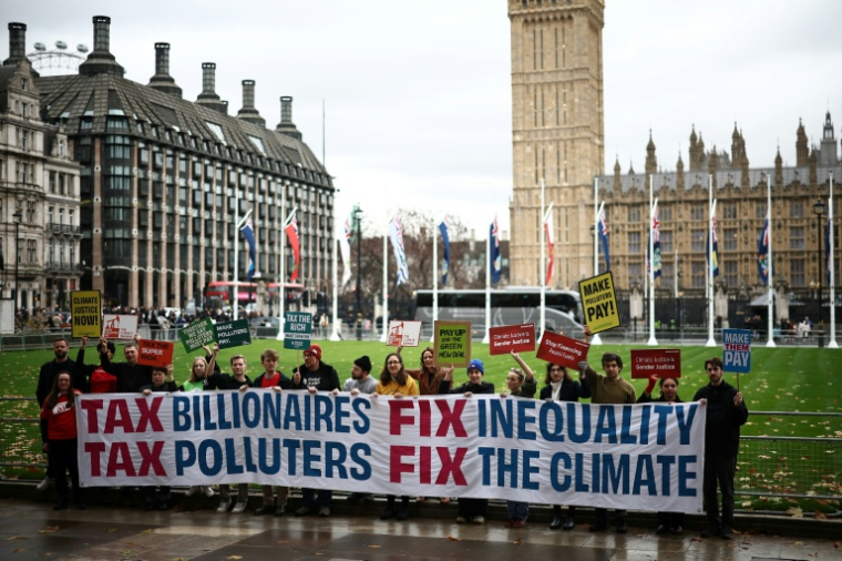 Des militants brandissent une banderole sur laquelle on peut lire "Taxer les milliardaires, corriger les inégalités, taxer les pollueurs, régler le problème du climat" devant le Parlement à Londres le 24 novembre 2025 en Angleterre ( AFP / HENRY NICHOLLS )