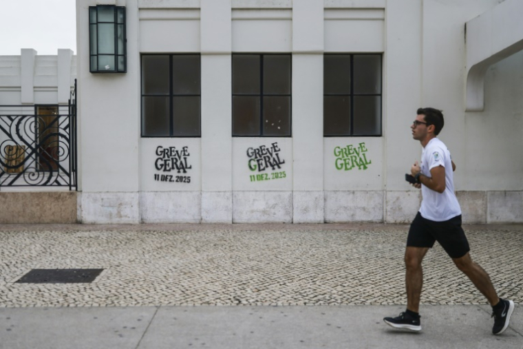 Un joggeur passe devant des graffitis appelant à la grève générale à Lisbonne le 11 décembre 2025  ( AFP / PATRICIA DE MELO MOREIRA )