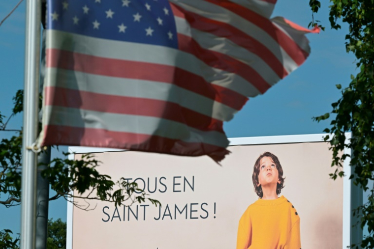 Une affiche publicitaire derrière un drapeau américain à côté de l'usine Saint-James, dans la Manche, le 22 mai 2025 ( AFP / Damien MEYER )