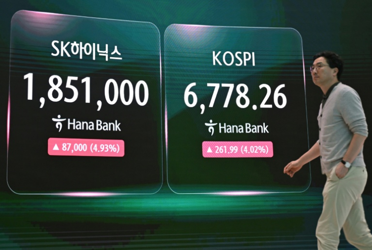 Un agent de change passe devant un écran affichant l'indice boursier de référence sud-coréen (d.) et le cours de l'action SK Hynix au siège de la Hana Bank, à Séoul, le 21 juillet 2026 ( AFP / Jung Yeon-je )