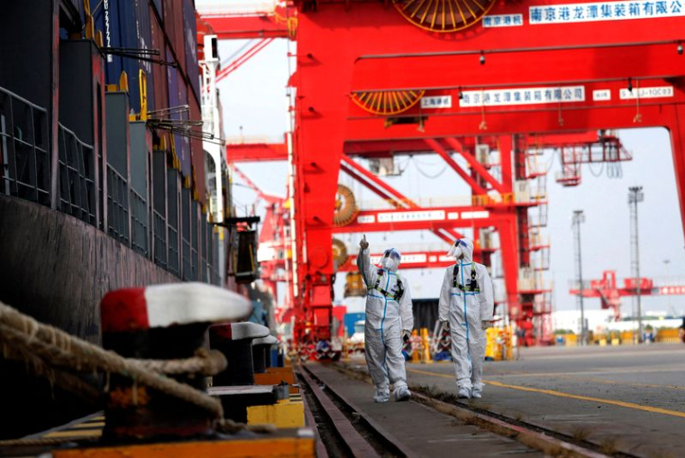 Des agents de la police des frontières en combinaison de protection patrouillent à côté d'un porte-conteneurs dans le port de Nanjing