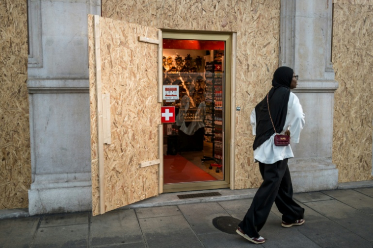 Une touriste marche devant un magasin de souvenir protégé par des panneaux de contreplaqué avant les manifestations anti-G7 prévues en marge du sommet à Evian, à Génève le 12 juin 2026 ( AFP / Fabrice COFFRINI )